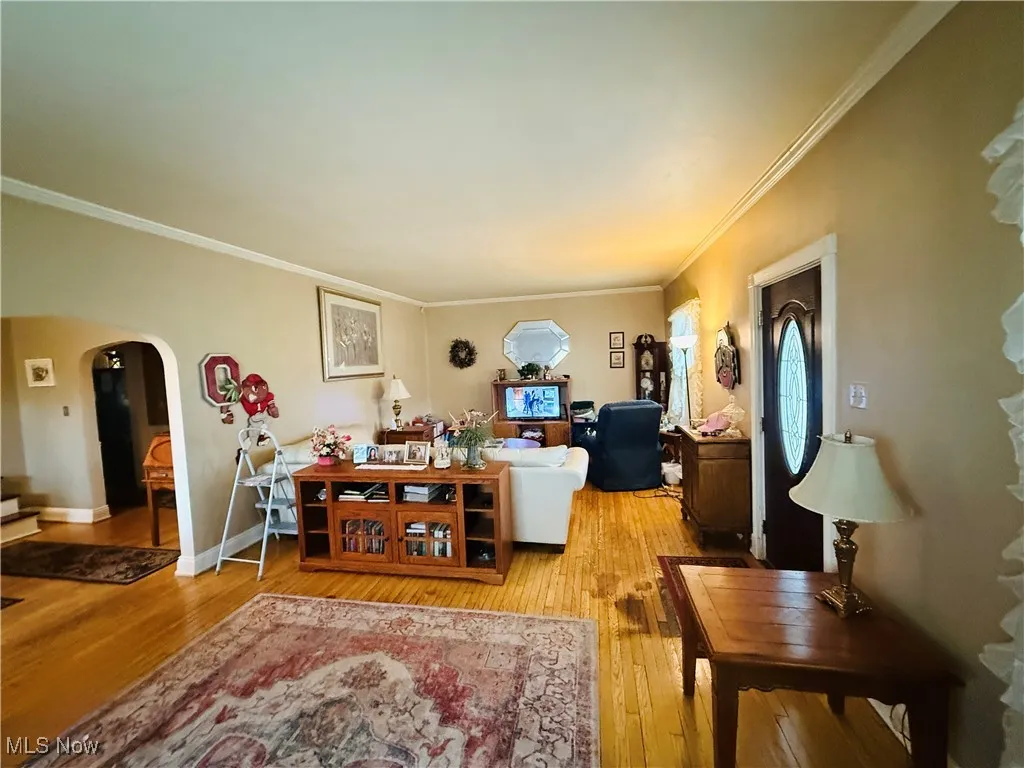 Living room featuring ornamental molding, baseboards, arched walkways, and wood finished floors