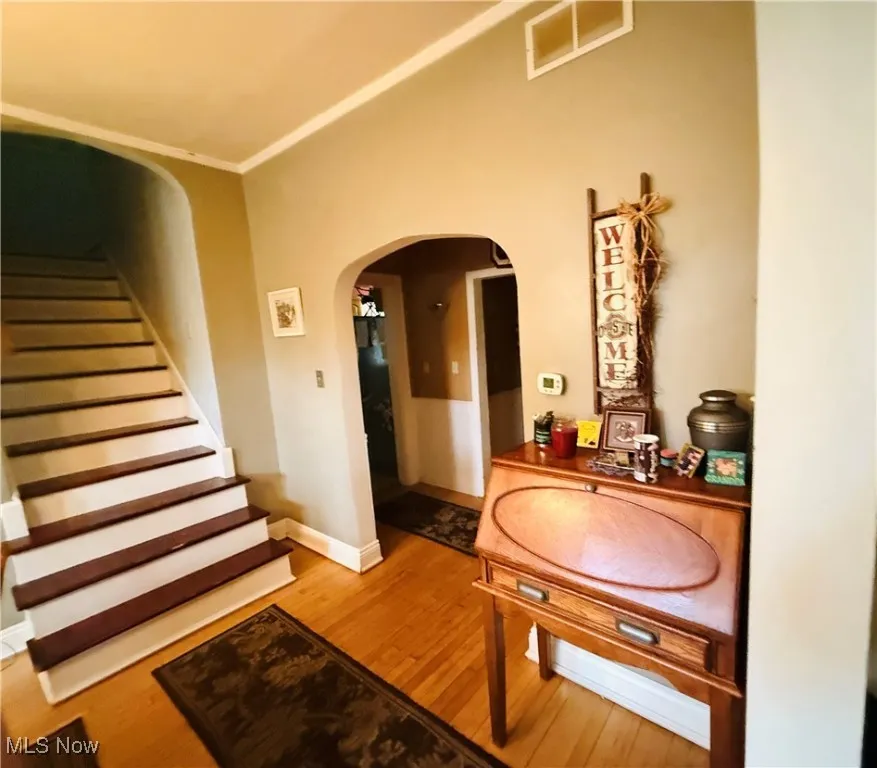 Hallway with arched walkways, visible vents, wood finished floors, stairs, and baseboards