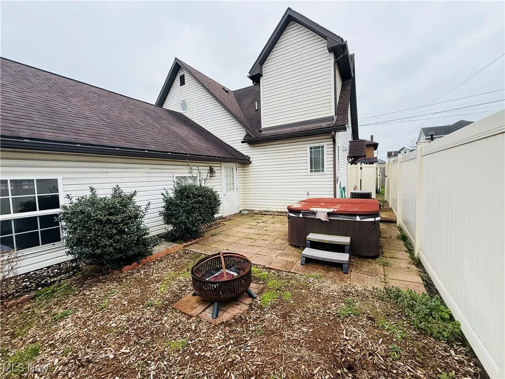 Rear view of property with a shingled roof, a hot tub, a patio area, an outdoor fire pit, and fence