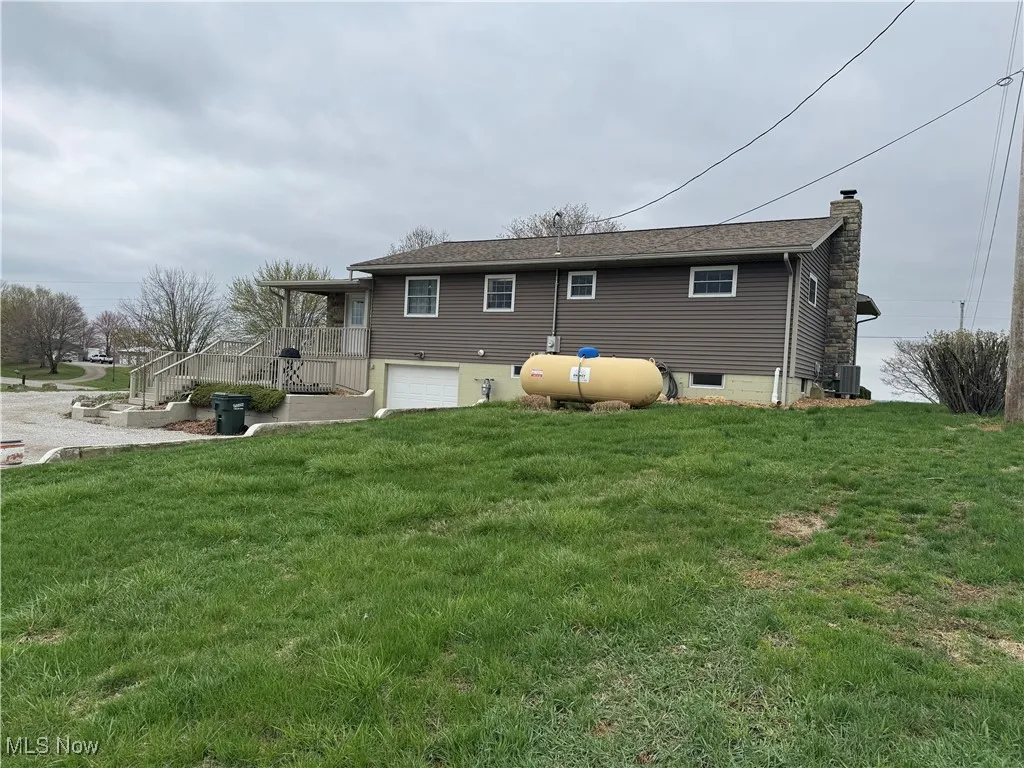Back of house with central air condition unit, a lawn, a garage, and a chimney