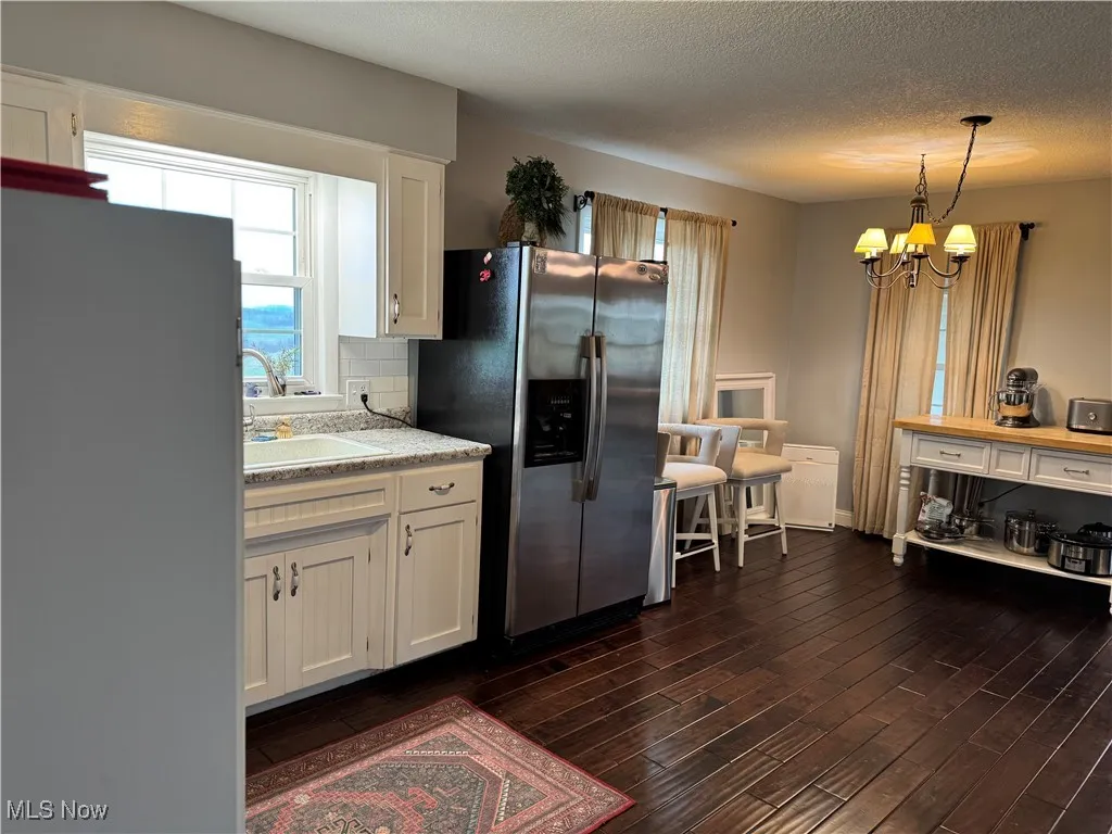 Kitchen featuring a chandelier, dark wood-style floors, white cabinetry, stainless steel refrigerator with ice dispenser, and a sink