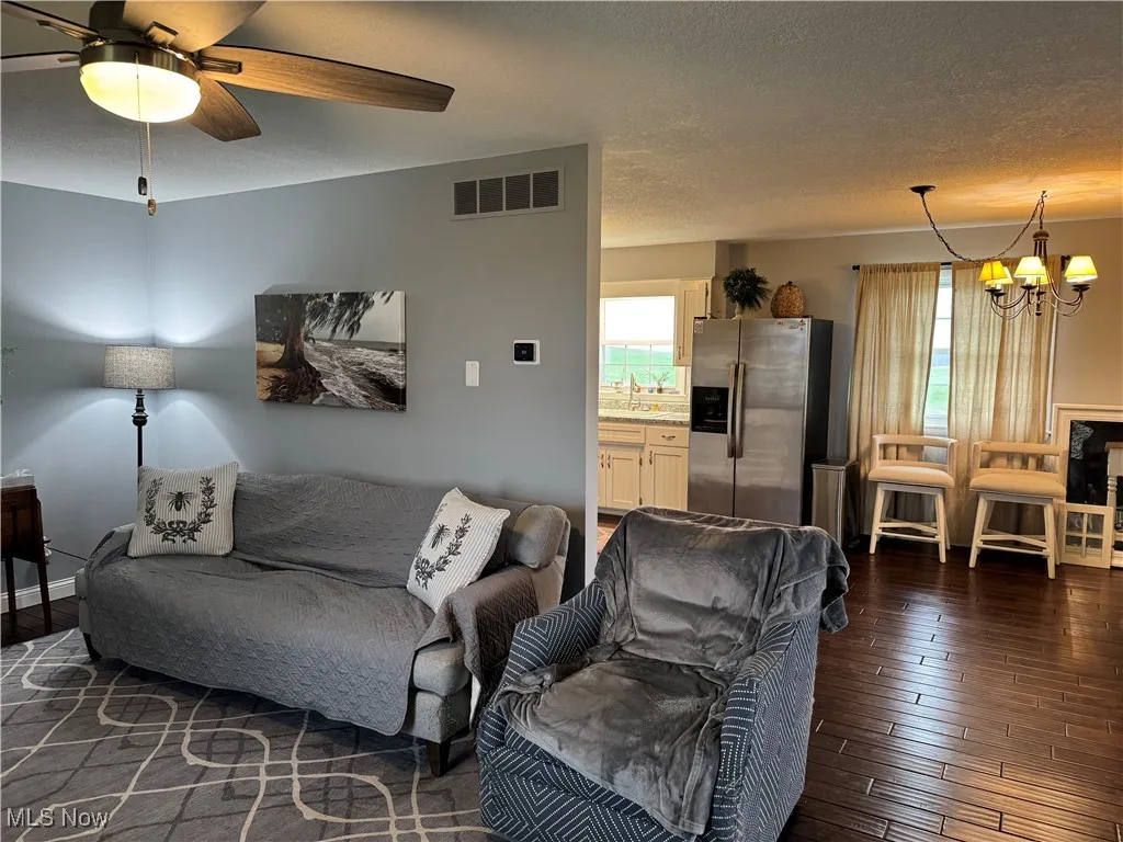 Living room with visible vents, a wealth of natural light, dark wood finished floors, and ceiling fan with notable chandelier