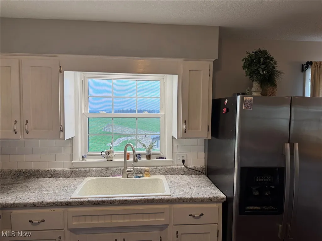 Kitchen featuring stainless steel fridge with ice dispenser, light countertops, white cabinetry, and a sink
