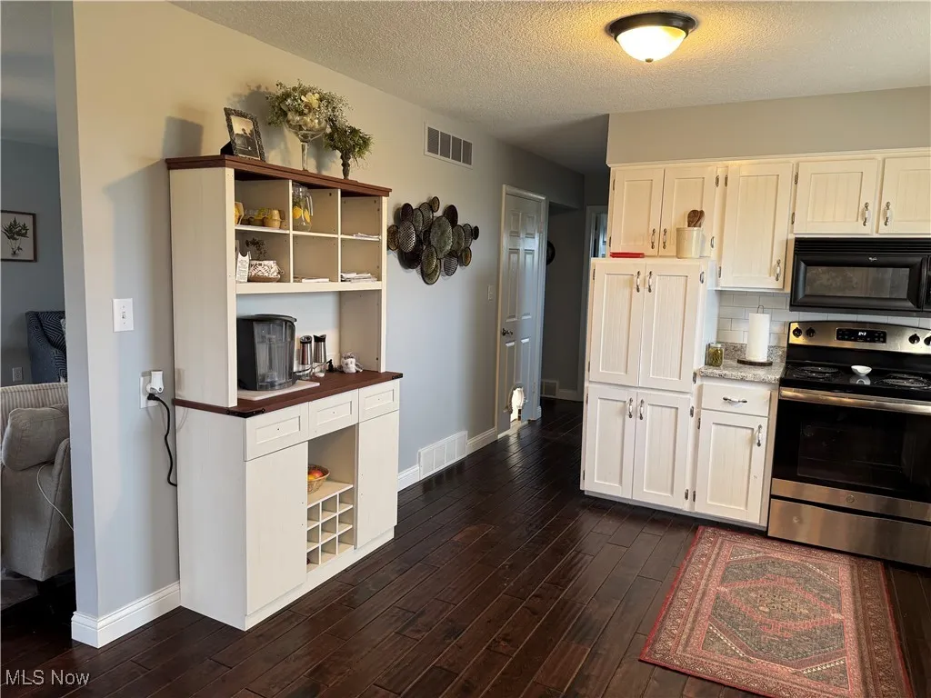 Kitchen featuring visible vents, black microwave, open shelves, and electric stove