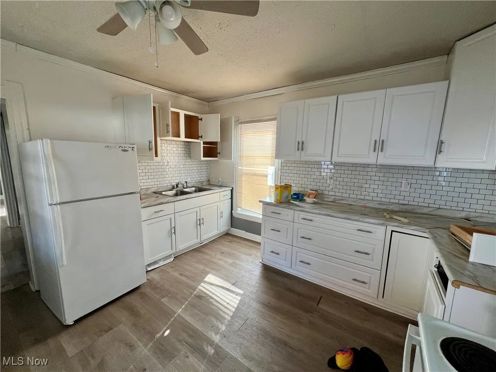 Kitchen featuring a sink, ornamental molding, white appliances, a textured ceiling, and white cabinetry