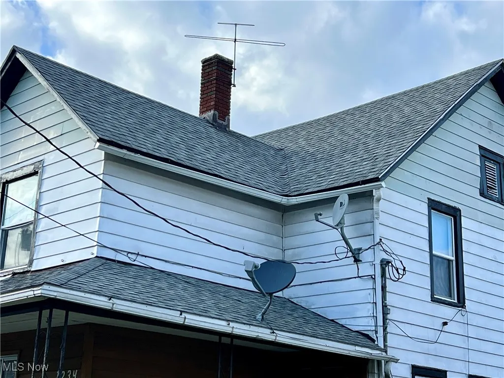 View of side of property with roof with shingles and a chimney