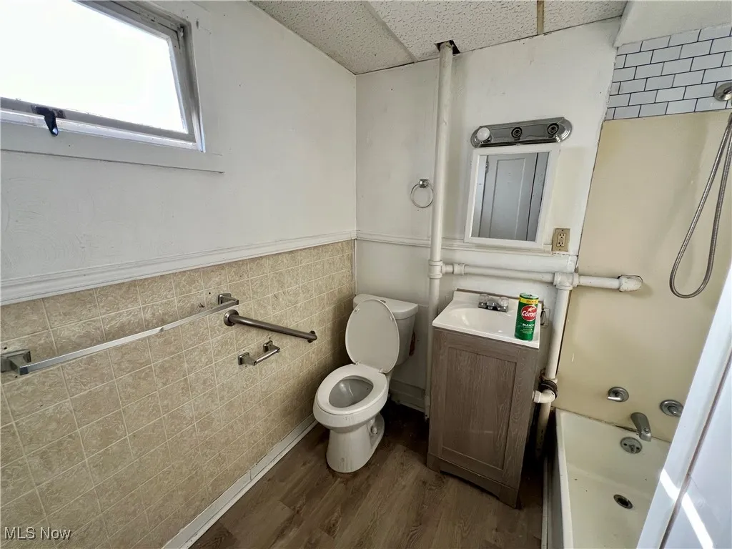 Full bathroom featuring toilet,  shower combination, vanity, wood finished floors, and a wainscoted wall