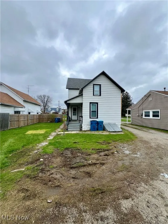 Back of property with a shingled roof, a yard, driveway, and fence