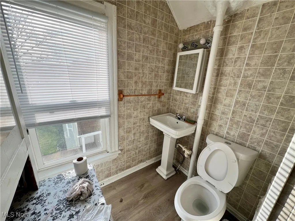 Half bath with vaulted ceiling, toilet, tile walls, a sink, and wood finished floors