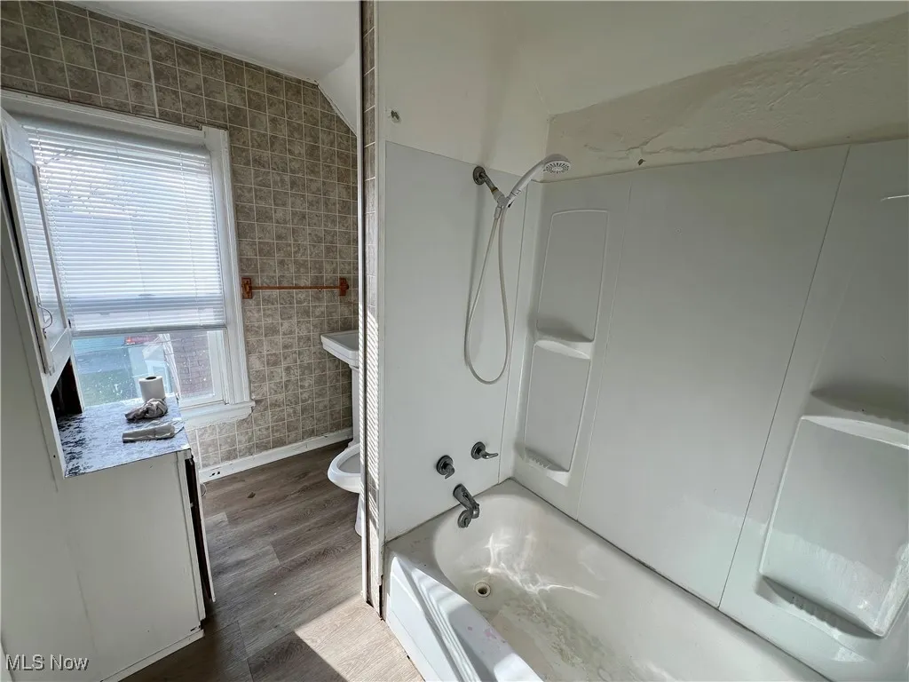 Full bath with tile walls, baseboards, wood finished floors, and shower / bathtub combination