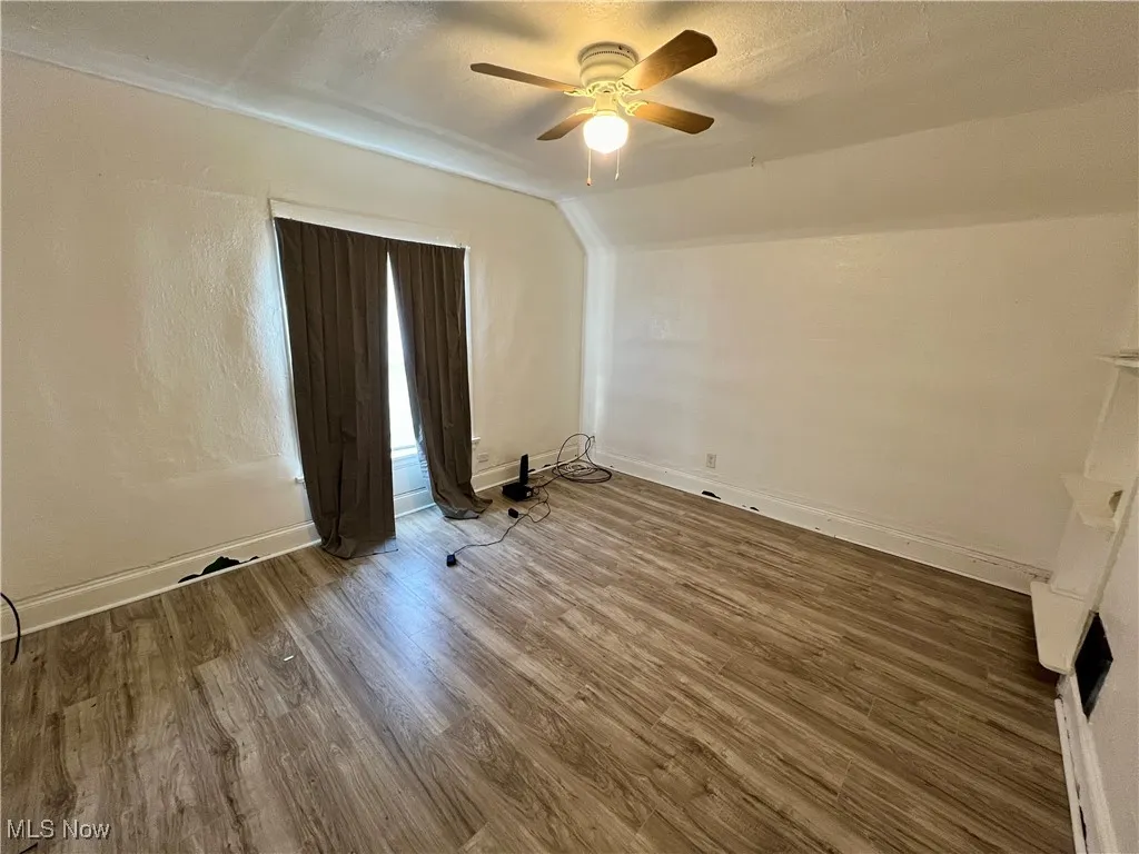 Empty room featuring baseboards, vaulted ceiling, a ceiling fan, and wood finished floors
