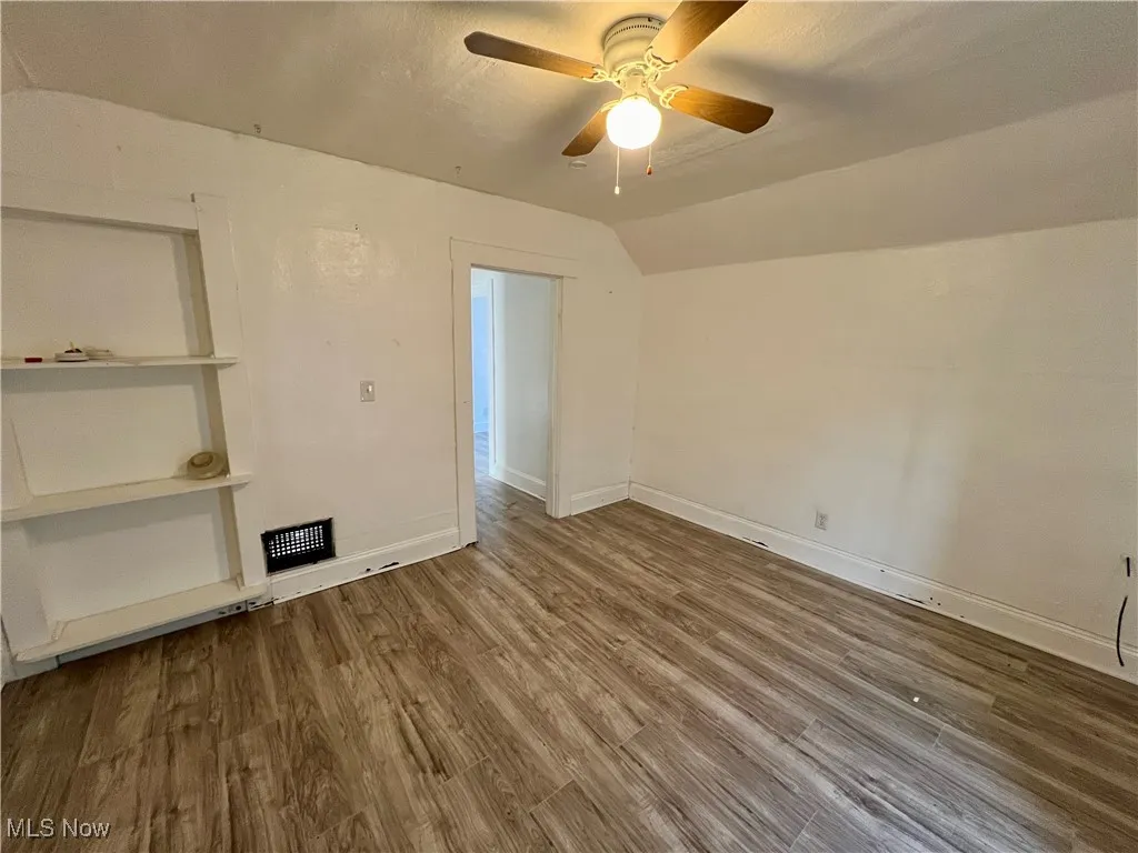 Unfurnished room with wood finished floors, baseboards, a ceiling fan, and vaulted ceiling