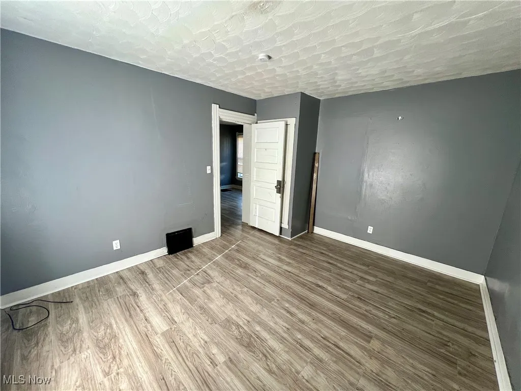 Unfurnished room featuring baseboards, a textured ceiling, and wood finished floors