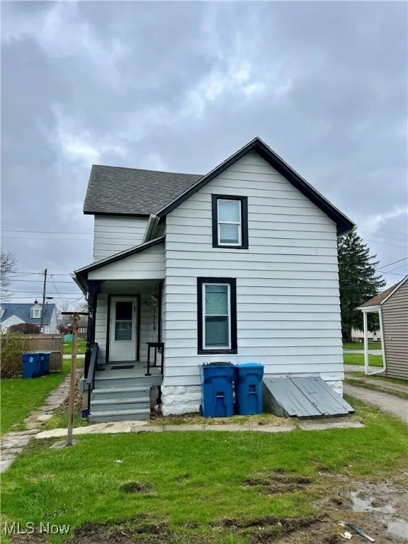 View of front of house with a shingled roof, covered porch, and a front lawn