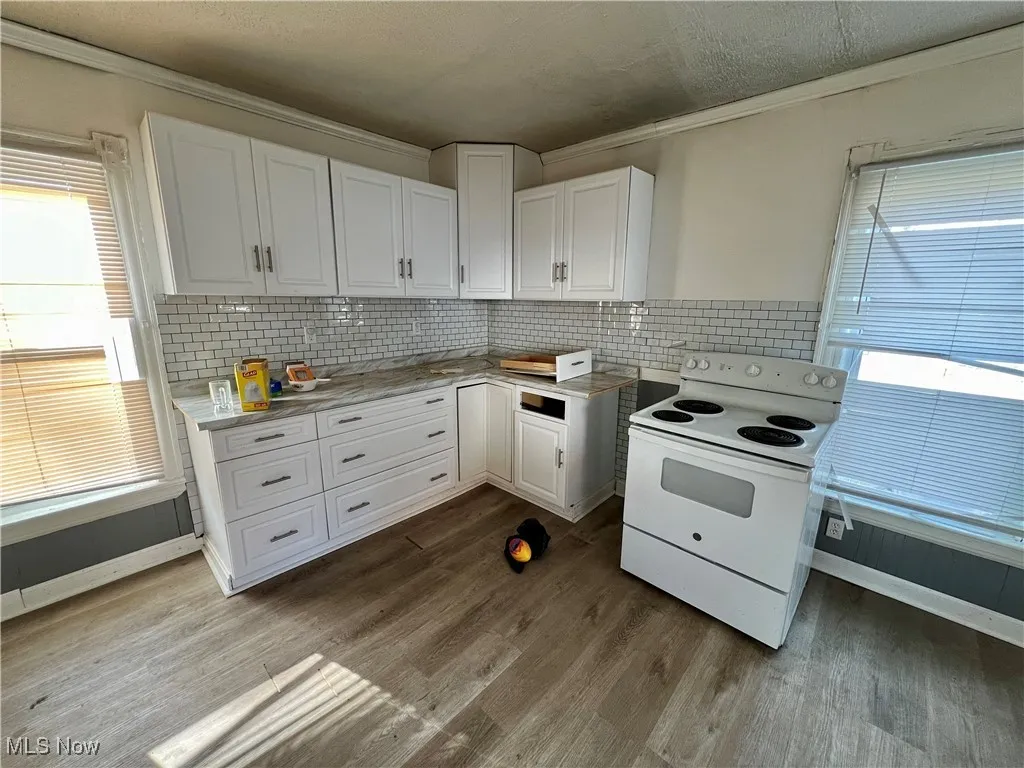 Kitchen with ornamental molding, white cabinetry, electric range, and dark wood-style floors