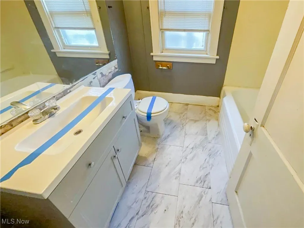 Full bathroom featuring a tub to relax in, vanity, toilet, marble finish floor, and baseboards