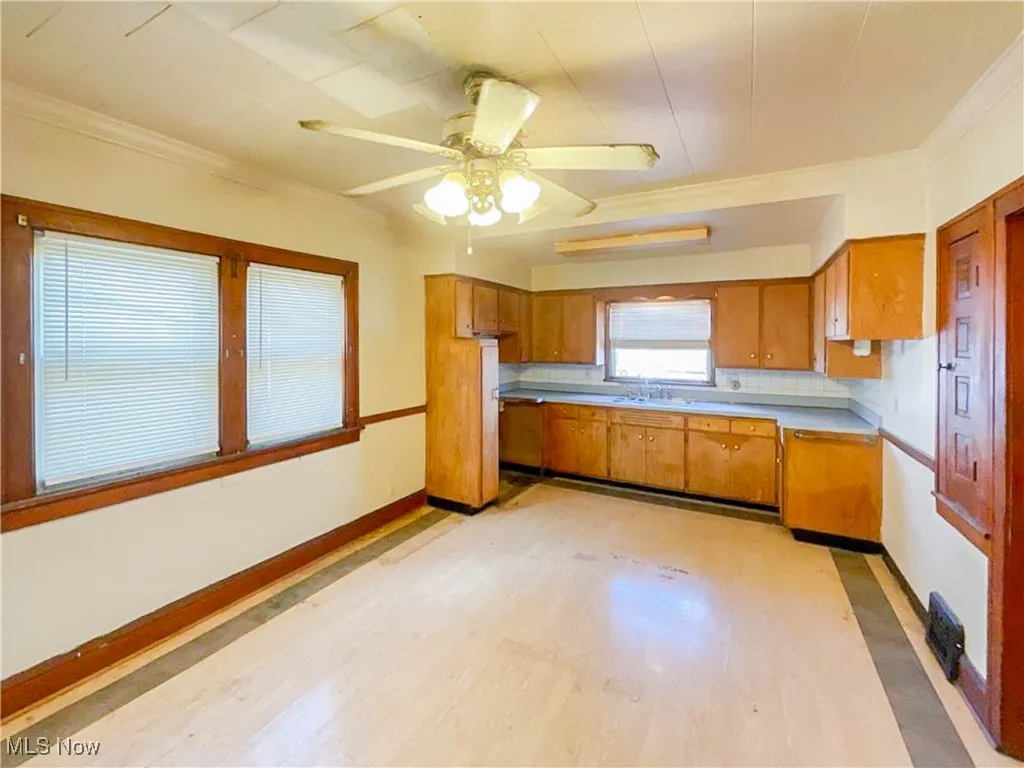 Kitchen with light wood-style flooring, brown cabinetry, ornamental molding, and ceiling fan