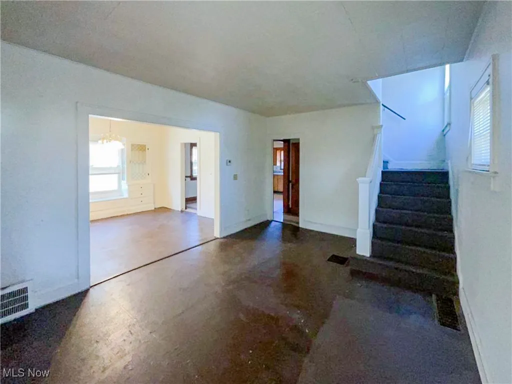 Unfurnished living room with baseboards, an inviting chandelier, finished concrete flooring, stairs, and visible vents