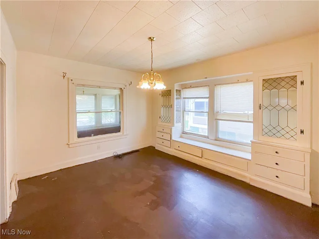 Unfurnished dining area with a healthy amount of sunlight, a notable chandelier, baseboards, and concrete floors