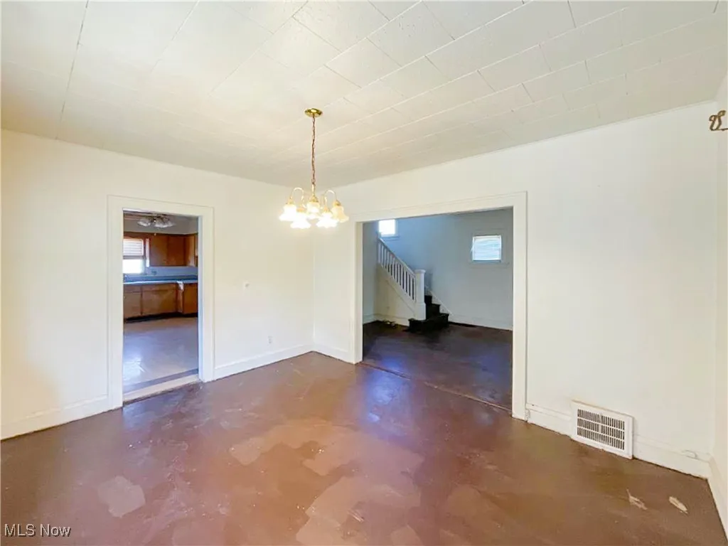 Unfurnished dining area featuring baseboards, an inviting chandelier, finished concrete flooring, stairs, and visible vents