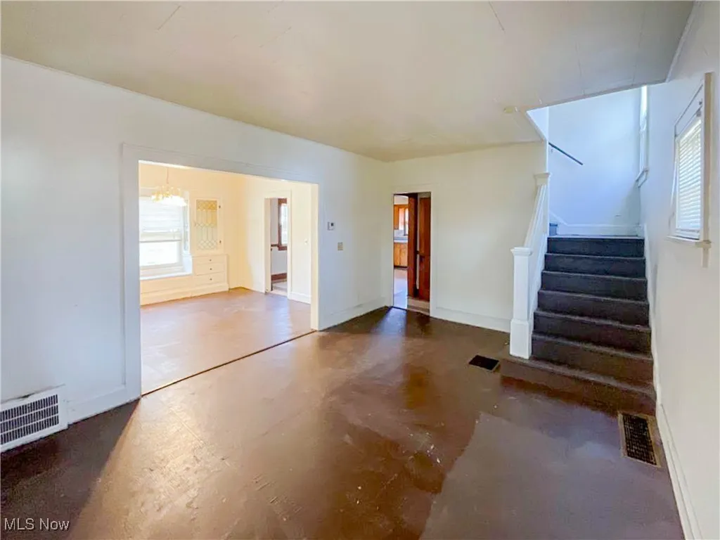 Unfurnished living room with stairway, visible vents, baseboards, and an inviting chandelier