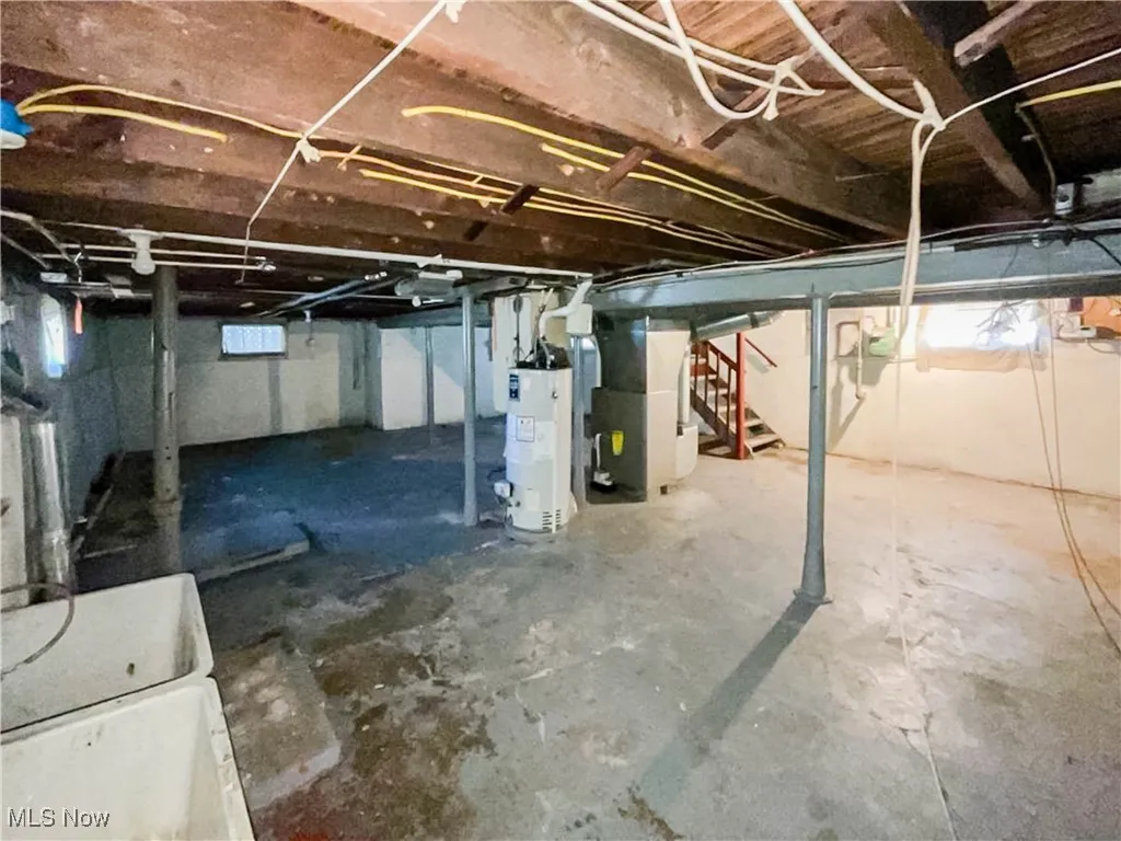 Unfinished basement featuring heating unit, stairway, and water heater