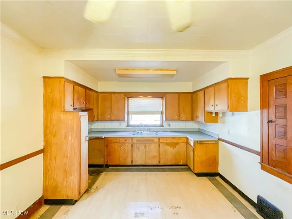 Kitchen featuring light wood-style flooring, a sink, light countertops, brown cabinets, and baseboards
