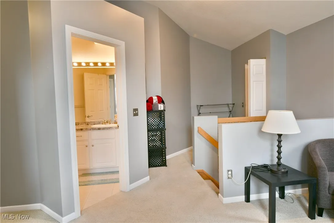 Hallway featuring a sink, baseboards, light colored carpet, and vaulted ceiling