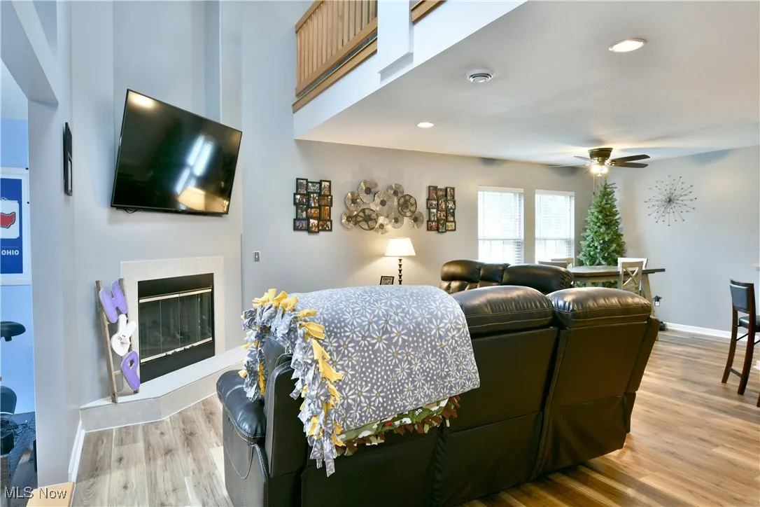 Living area with baseboards, a ceiling fan, a glass covered fireplace, and wood finished floors