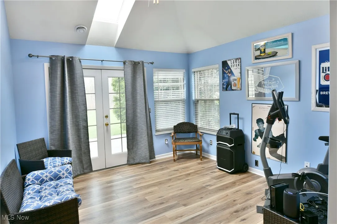 Sitting room featuring french doors, baseboards, light wood finished floors, and lofted ceiling with skylight