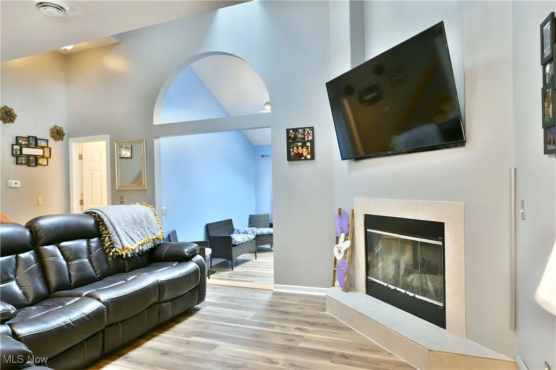 Living area with a tiled fireplace, high vaulted ceiling, and wood finished floors