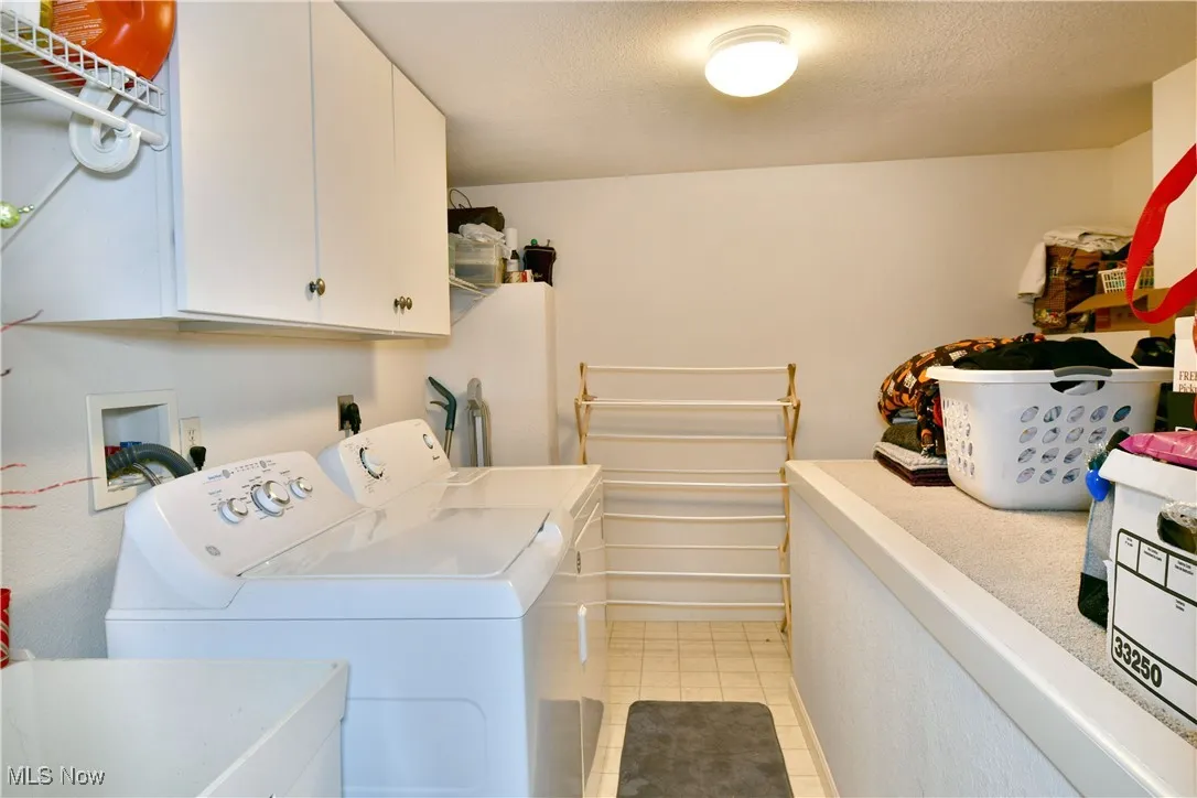 Laundry area with light tile patterned floors, washing machine and dryer, a textured ceiling, and cabinet space