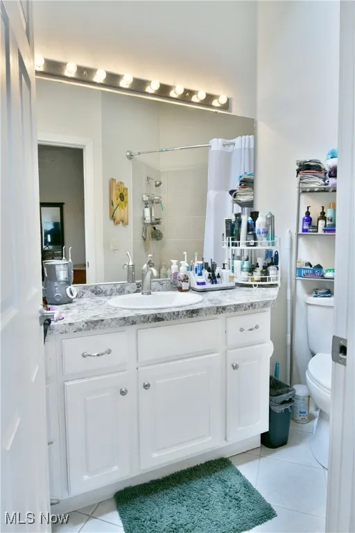 Full bathroom featuring toilet, curtained shower, vanity, and tile patterned flooring