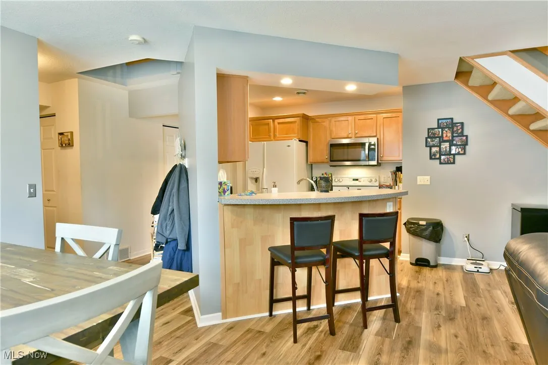 Kitchen featuring light wood-type flooring, a kitchen breakfast bar, a peninsula, stainless steel microwave, and white refrigerator with ice dispenser