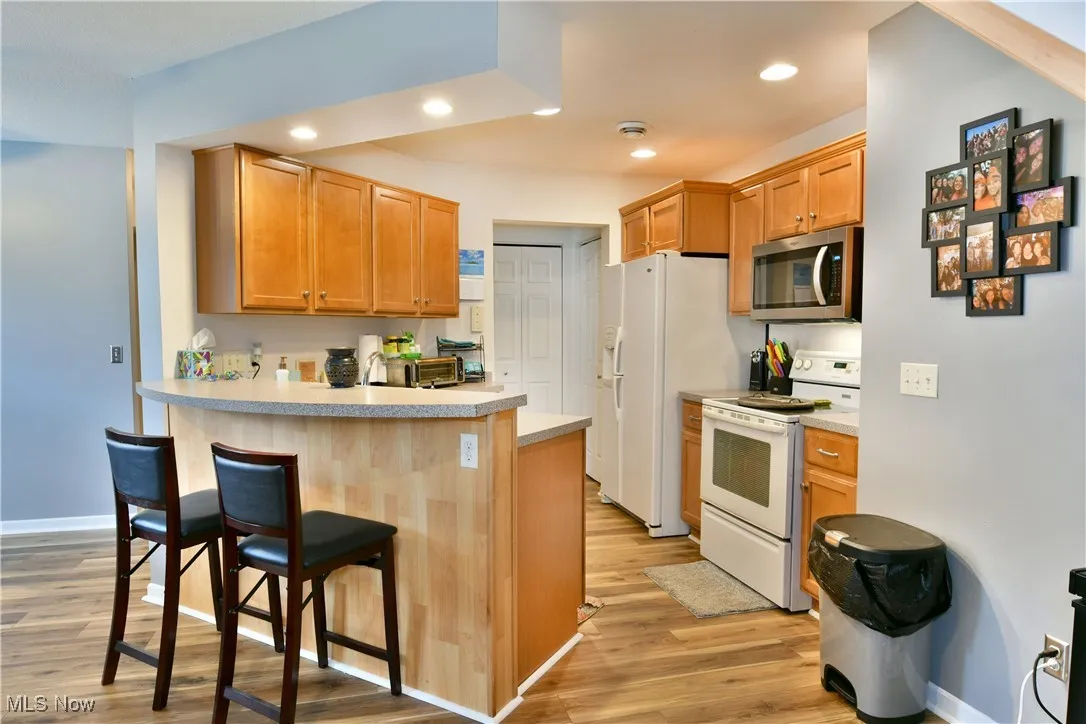 Kitchen with light countertops, a breakfast bar, white appliances, a peninsula, and light wood finished floors