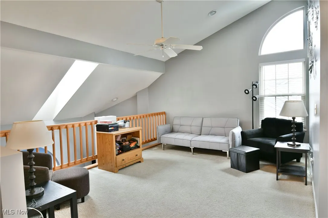 Living area with high vaulted ceiling, carpet, a ceiling fan, and a skylight