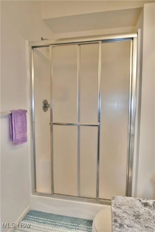 Full bath with toilet, baseboards, and a shower with door