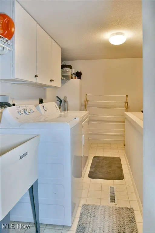 Laundry area featuring light tile patterned floors, separate washer and dryer, visible vents, a sink, and cabinet space