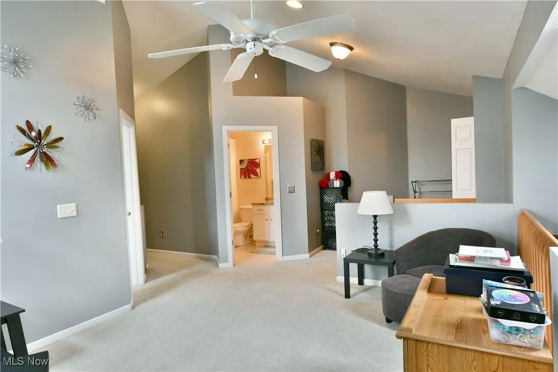Office space featuring baseboards, a ceiling fan, high vaulted ceiling, and light carpet