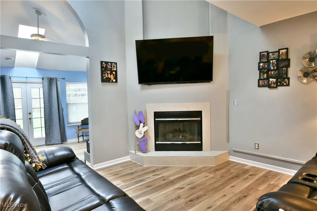 Living room with baseboards, a glass covered fireplace, wood finished floors, and lofted ceiling