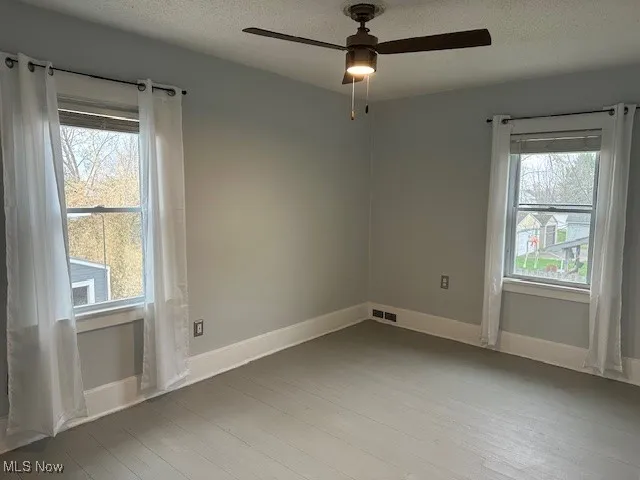 Spare room featuring visible vents, baseboards, a ceiling fan, and wood finished floors
