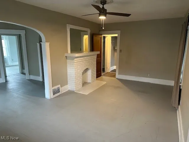 Unfurnished living room featuring visible vents, baseboards, arched walkways, a ceiling fan, and finished concrete floors