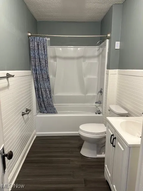 Full bath featuring shower / bath combo, wainscoting, a textured ceiling, and wood finished floors