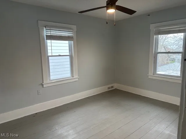 Empty room with visible vents, hardwood / wood-style flooring, baseboards, and ceiling fan