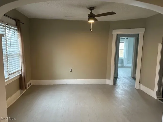 Spare room featuring ceiling fan, arched walkways, a textured ceiling, wood finished floors, and baseboards