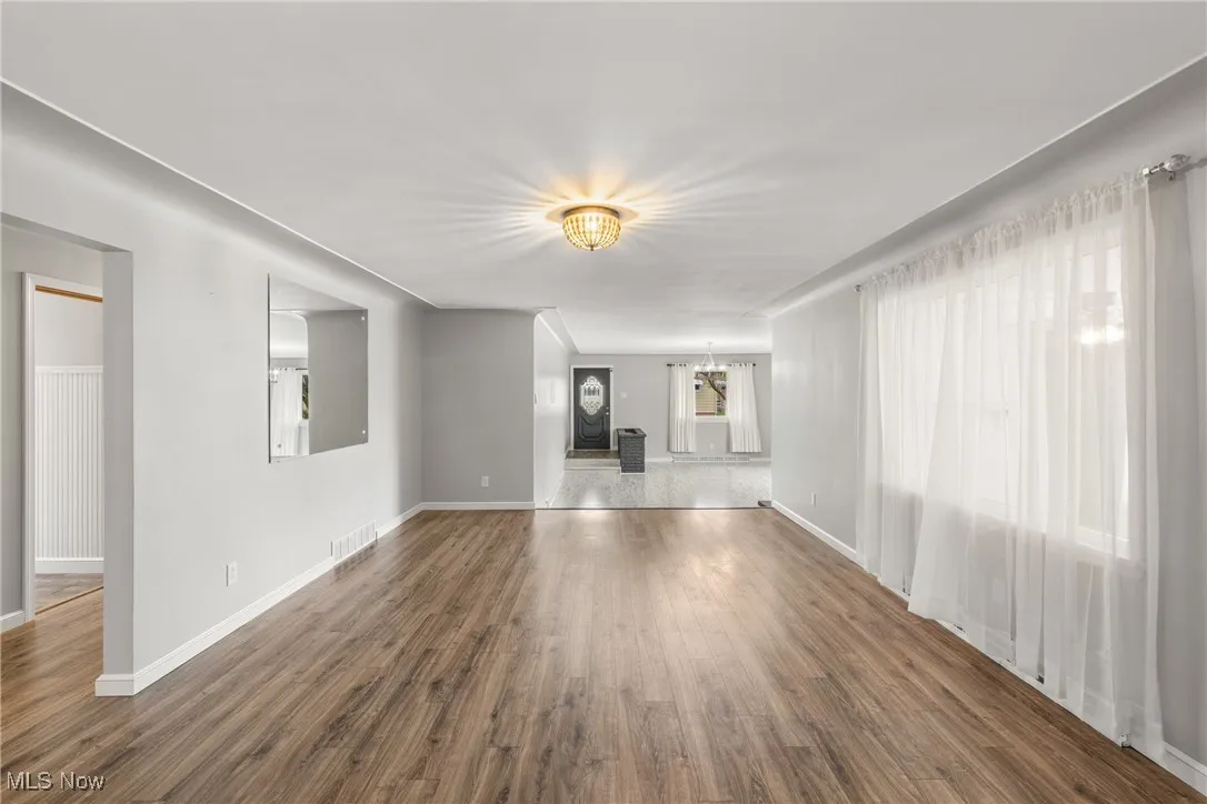 Unfurnished living room with visible vents, baseboards, an inviting chandelier, and wood finished floors