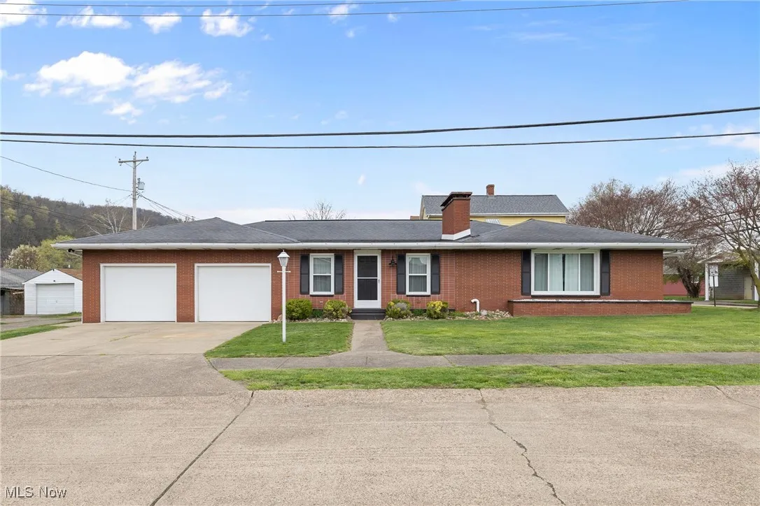 Ranch-style home featuring a front lawn, brick siding, a chimney, a garage, and driveway