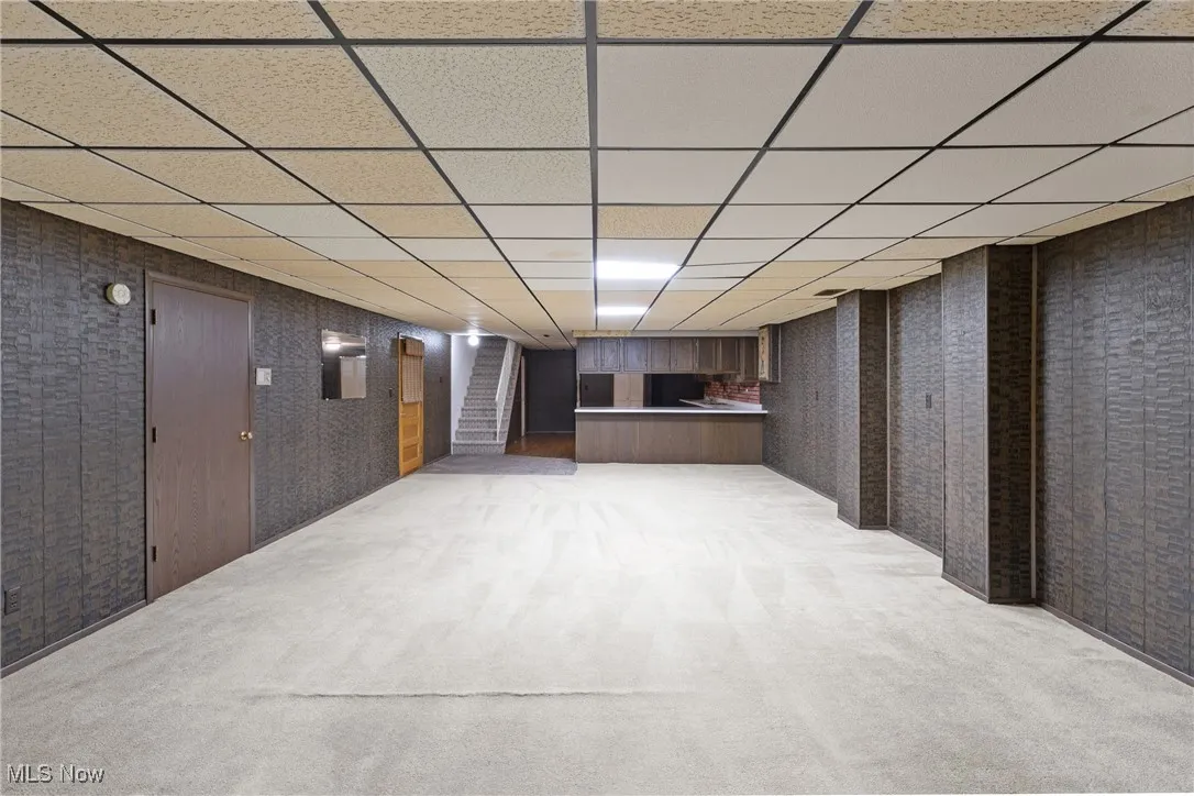 Finished below grade area with light colored carpet, a drop ceiling, and stairs