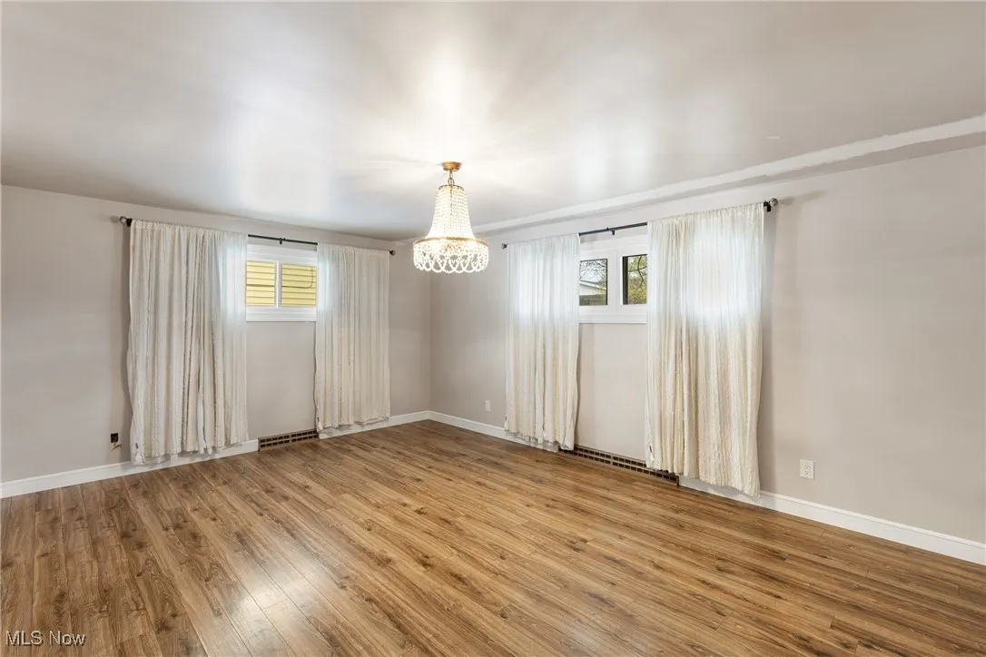 Unfurnished room with baseboards, an inviting chandelier, wood finished floors, and a healthy amount of sunlight