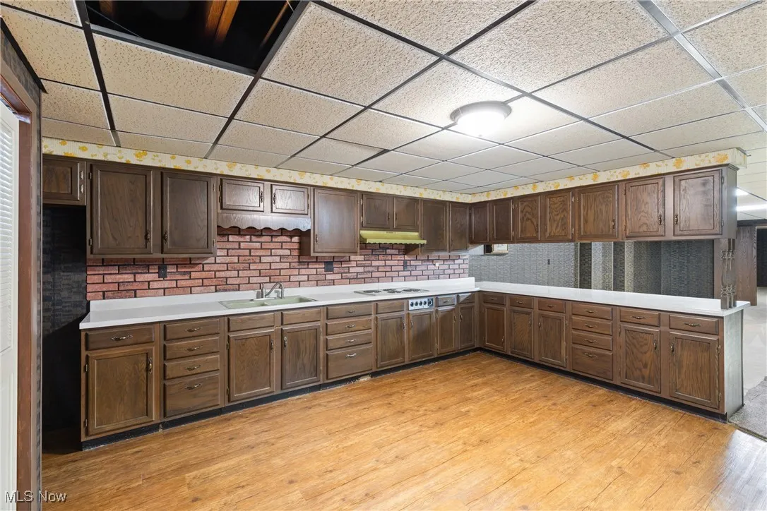 Kitchen featuring light countertops, white cooktop, under cabinet range hood, light wood finished floors, and a sink